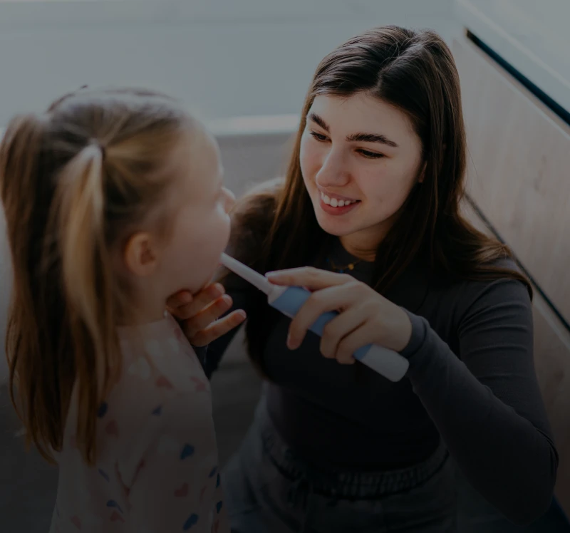 Smiling woman brushing girl's teeth